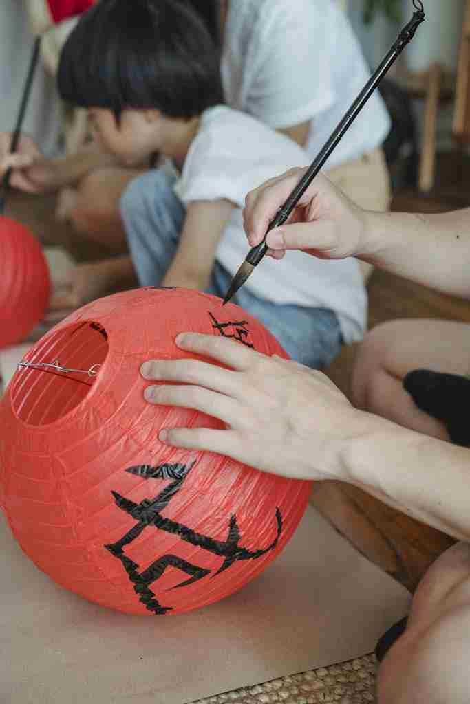 Close-up of hands painting Chinese characters on red paper lanterns indoors.