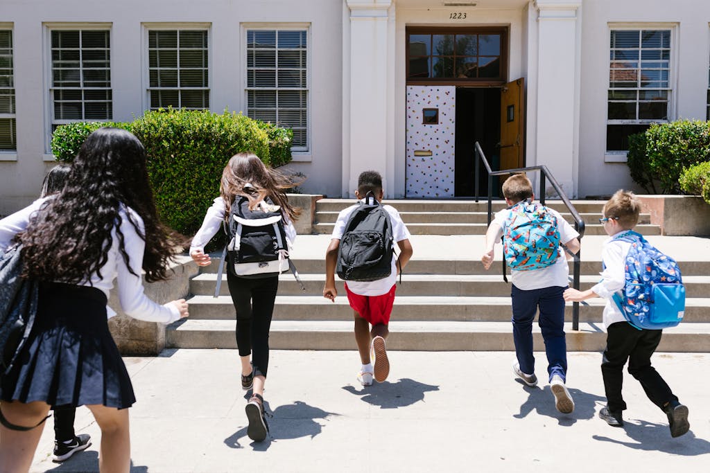 Group of students with backpacks running into school, captured from behind, showing excitement.